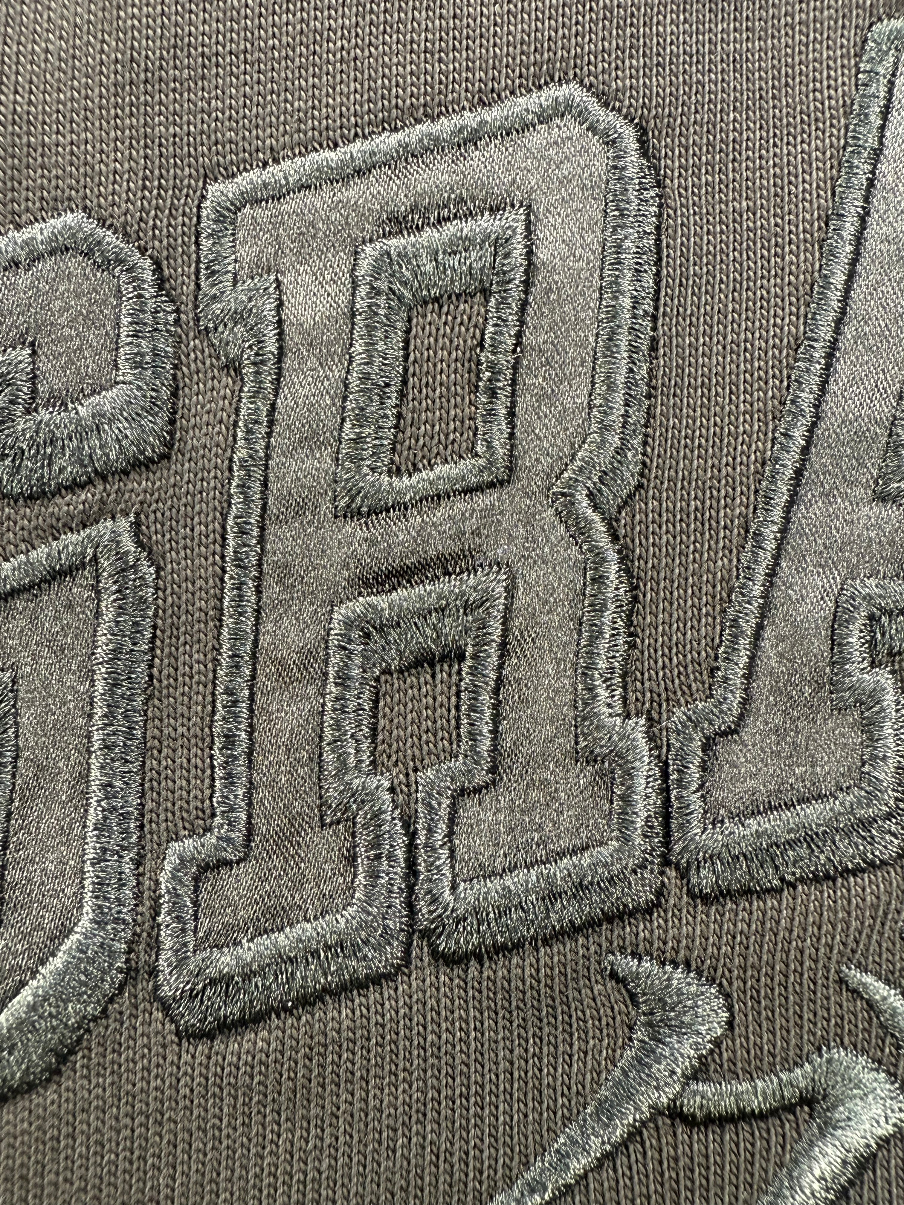 Close-up of embroidered grappler satin text and katakana on a black jersey knit tee shirt