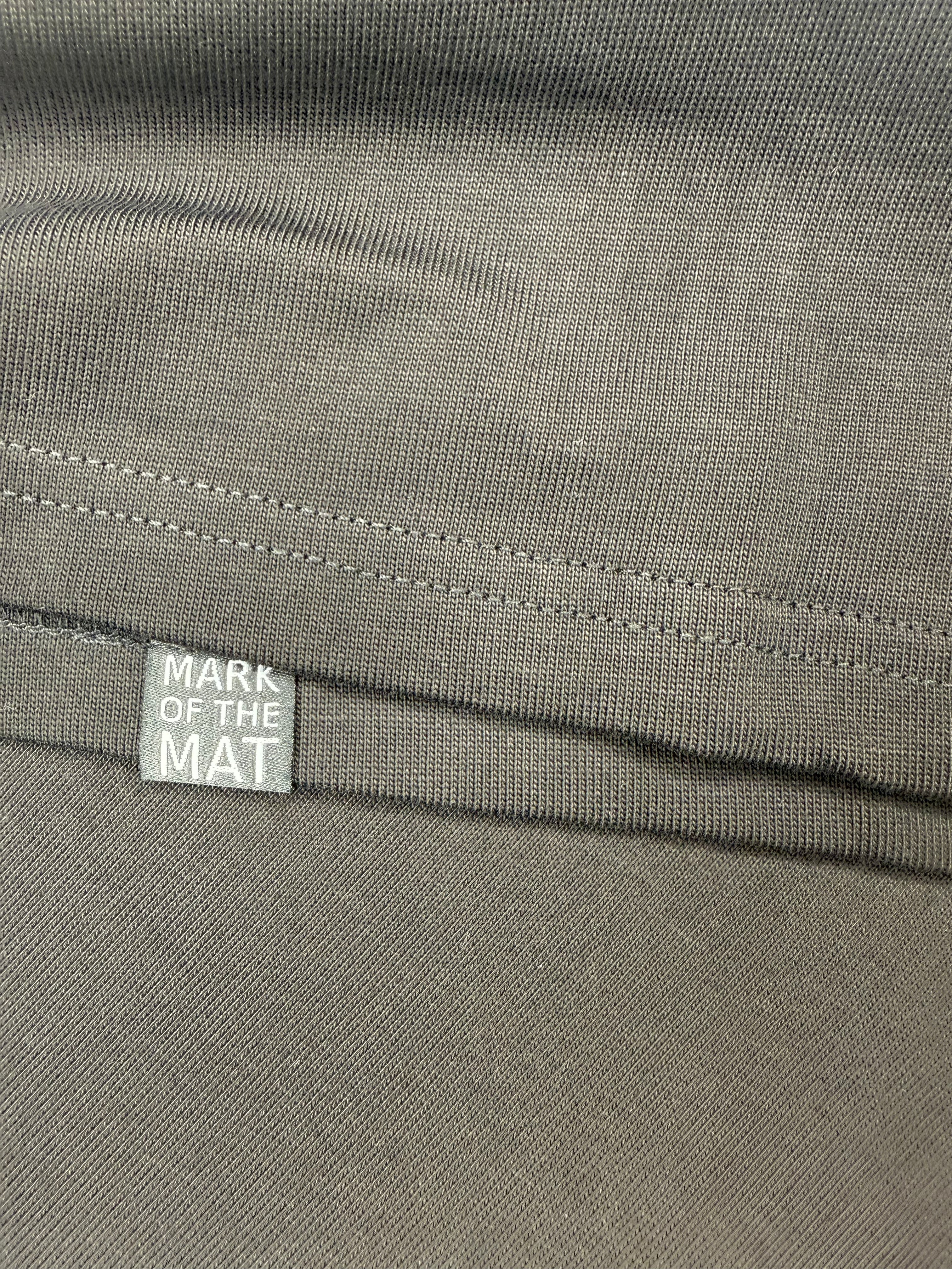 Close-up of a black tee shirt fabric with hidden detail 'Mark of the Mat' woven label on hem
